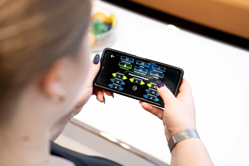Smartphone zeigt EMS App für Terminbuchung und Trainingsfortschritt.